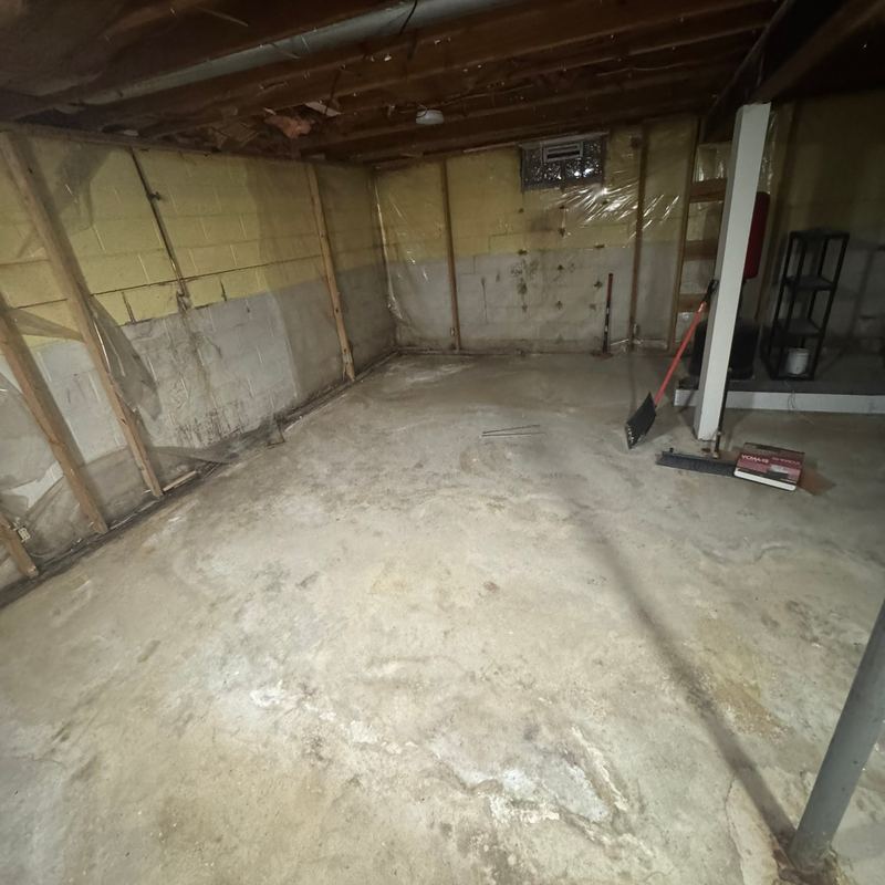An empty unfinished basement with bare block walls, a concrete floor and open ceiling joists