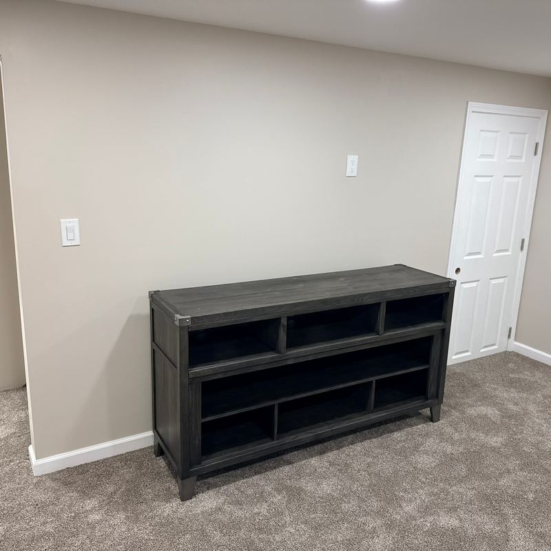 A finished room with beige walls, carpet, white trim and a dark dresser