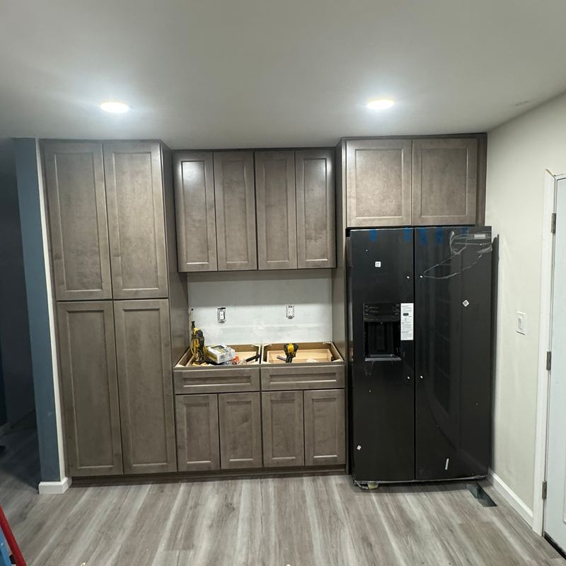A kitchen with new wood cabinets, a black refrigerator and plank flooring